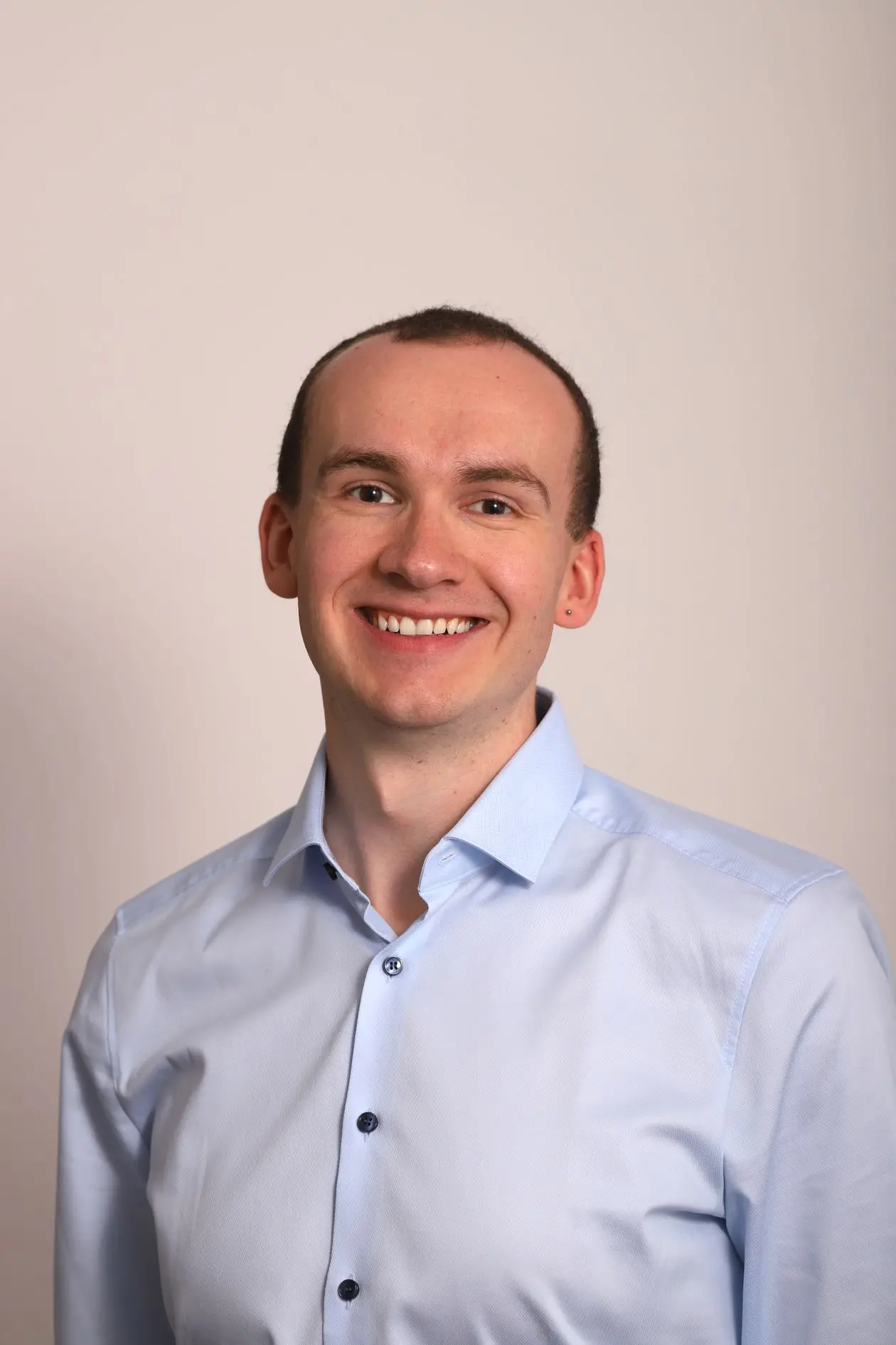 Professional portrait of a smiling man in business attire against a studio background, consistent corporate headshot style
