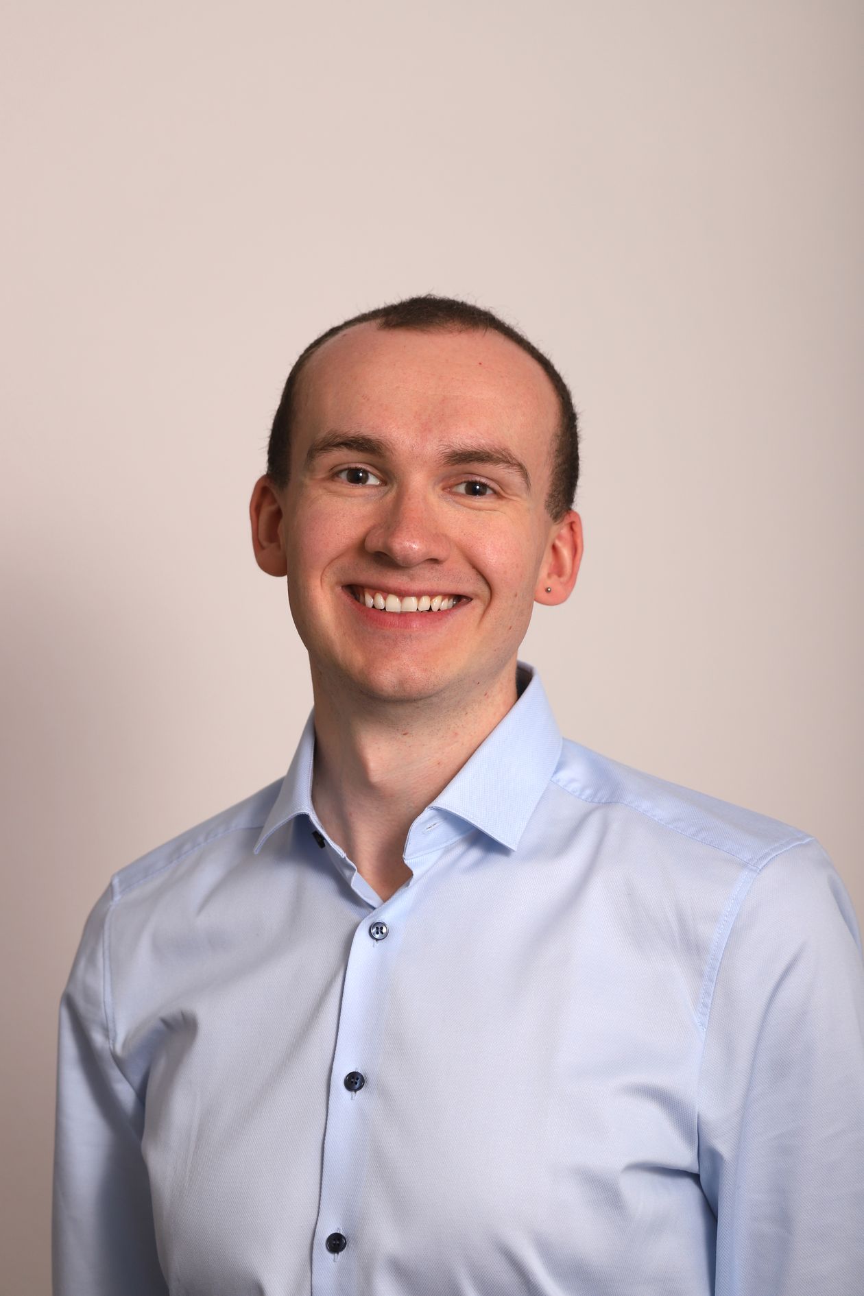 Professional portrait of a smiling man in business attire against a studio background, consistent corporate headshot style