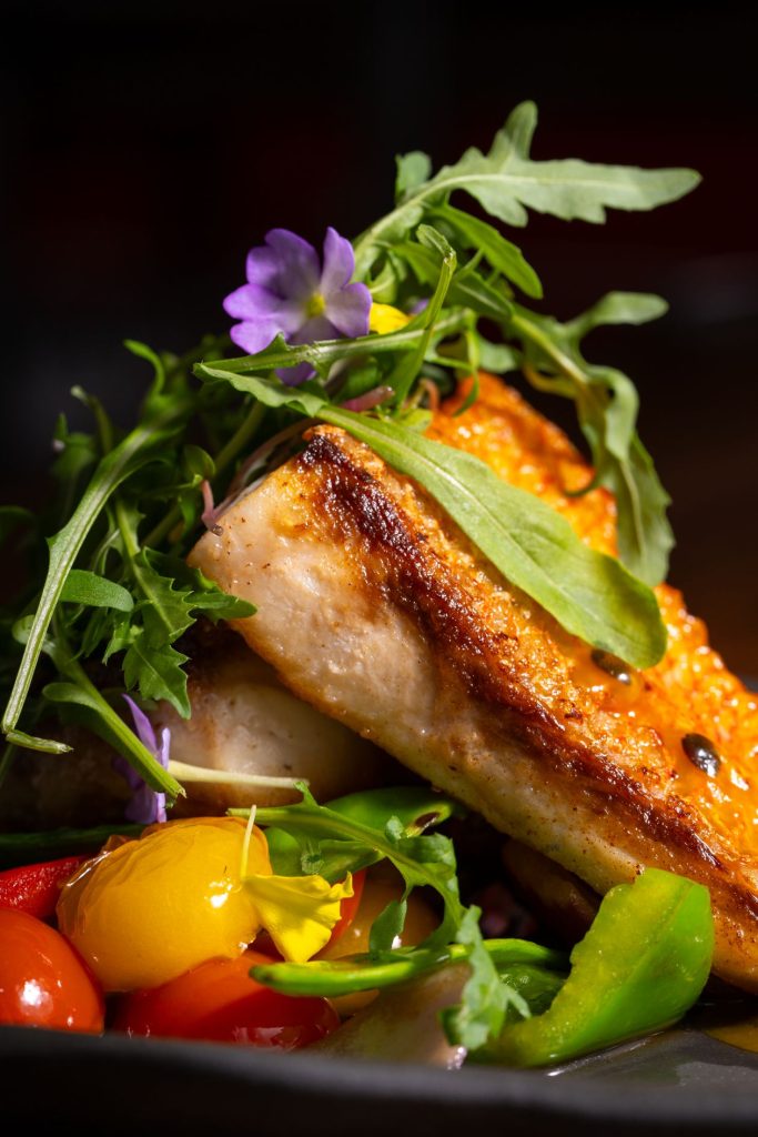 Grilled salmon with fresh salad and edible flowers, professional restaurant menu photography